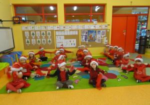 Dzieci siedzą w czterech rzędach, unoszą czerwone chusteczki na boki.